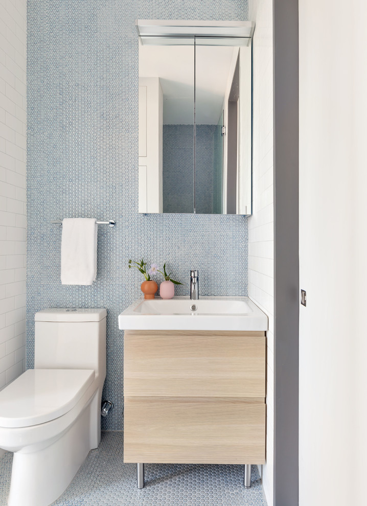 Photo of a scandinavian powder room in New York with flat-panel cabinets, light wood cabinets, a one-piece toilet, blue tile, mosaic tile, blue walls, mosaic tile floors and blue floor.