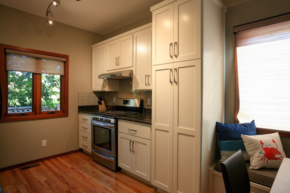 Example of a mid-sized transitional galley medium tone wood floor and beige floor eat-in kitchen design with shaker cabinets, white cabinets, granite countertops, green backsplash, subway tile backsplash, stainless steel appliances and no island