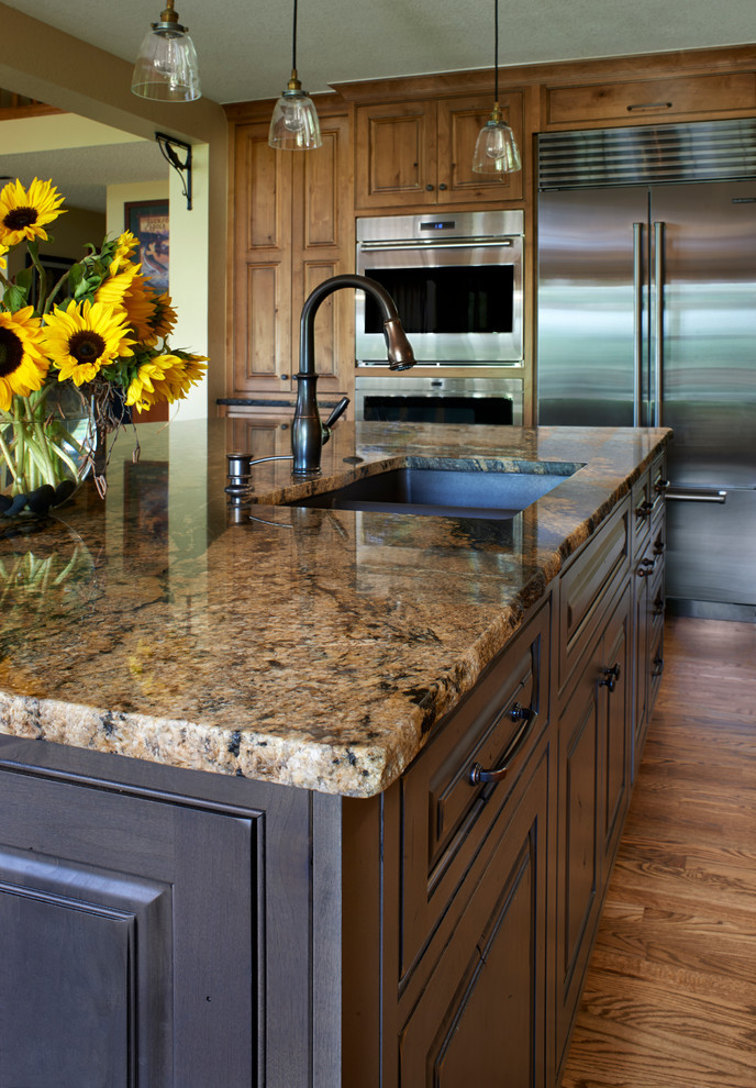 Inspiration for a large rustic l-shaped medium tone wood floor open concept kitchen remodel in Denver with a double-bowl sink, raised-panel cabinets, light wood cabinets, granite countertops, brown backsplash, porcelain backsplash, stainless steel appliances and an island