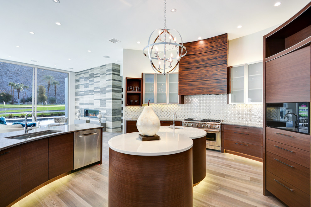 Photo of a contemporary open plan kitchen in Los Angeles with an undermount sink, stainless steel appliances, multiple islands, flat-panel cabinets, medium wood cabinets, metallic splashback and light hardwood floors.