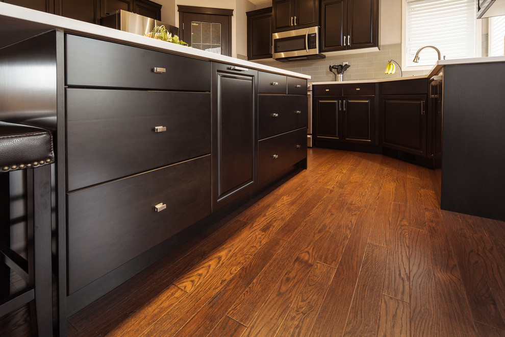 Example of a large transitional u-shaped dark wood floor and brown floor eat-in kitchen design in Calgary with a double-bowl sink, raised-panel cabinets, dark wood cabinets, quartz countertops, gray backsplash, ceramic backsplash, stainless steel appliances and an island