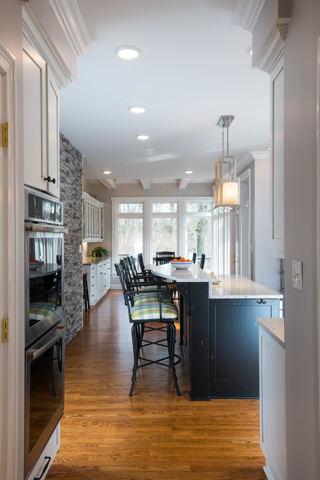 Eat-in kitchen - modern galley medium tone wood floor eat-in kitchen idea with an undermount sink, recessed-panel cabinets, white cabinets, granite countertops, white backsplash, ceramic backsplash, stainless steel appliances and an island