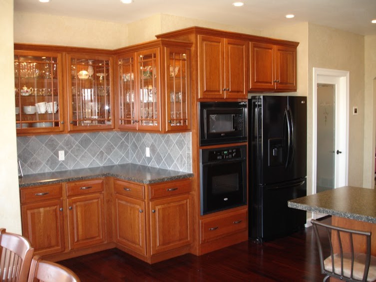 Eat-in kitchen - large u-shaped dark wood floor eat-in kitchen idea with a drop-in sink, raised-panel cabinets, medium tone wood cabinets, laminate countertops, gray backsplash, stone tile backsplash, black appliances and an island