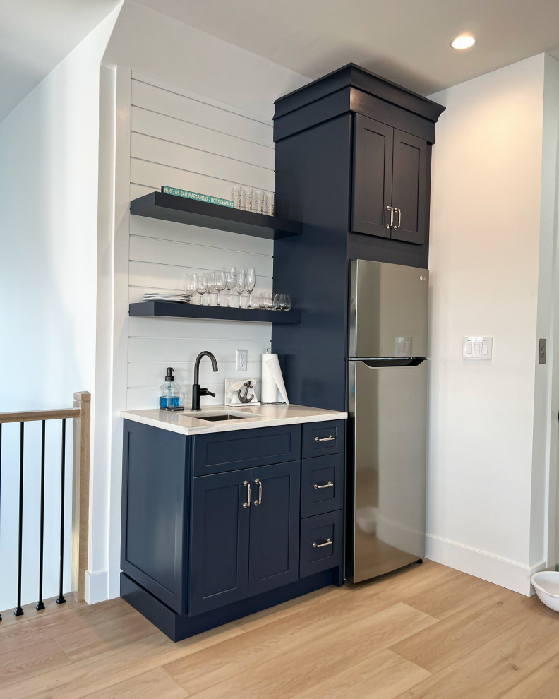 Small beach style wet bar in Other with an undermount sink, shaker cabinets, blue cabinets, quartz benchtops, white splashback, shiplap splashback, laminate floors, brown floor and white benchtop.