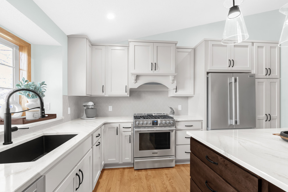 Mid-sized transitional l-shaped light wood floor and beige floor kitchen photo in Minneapolis with an undermount sink, shaker cabinets, white cabinets, quartz countertops, white backsplash, ceramic backsplash, stainless steel appliances, an island and white countertops