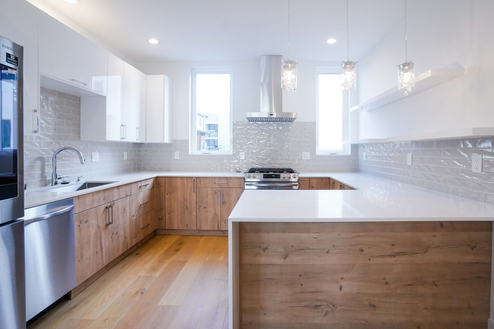 Bild på ett stort funkis vit vitt kök, med en undermonterad diskho, öppna hyllor, vita skåp, bänkskiva i kvartsit, grått stänkskydd, stänkskydd i keramik, rostfria vitvaror, mellanmörkt trägolv, en köksö och brunt golv