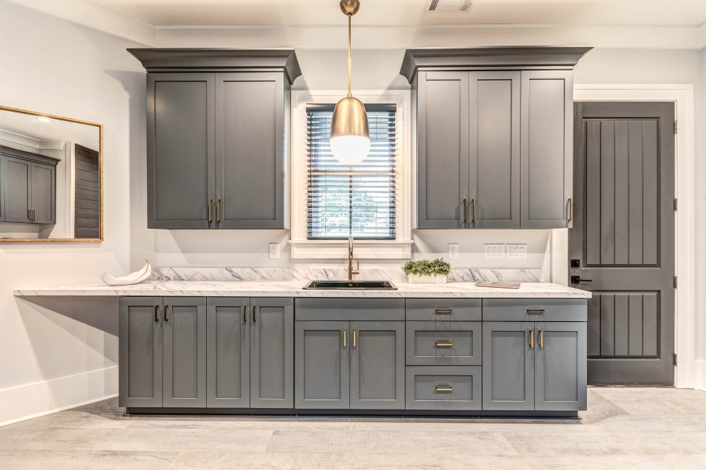 Photo of an expansive arts and crafts galley utility room in Atlanta with a drop-in sink, shaker cabinets, grey cabinets, laminate benchtops, grey walls, porcelain floors, a side-by-side washer and dryer, grey floor and white benchtop.