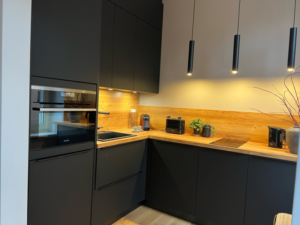 Bild på ett litet funkis kök, med en enkel diskho, släta luckor, svarta skåp, träbänkskiva, svarta vitvaror och mellanmörkt trägolv