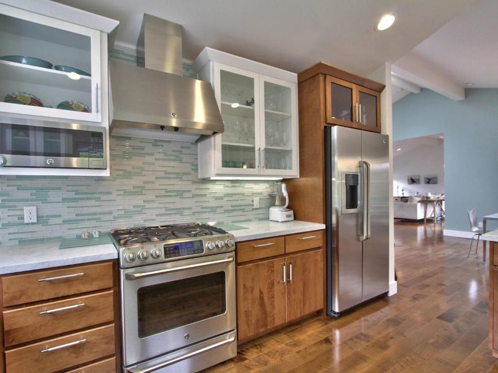 This is an example of a mid-sized beach style u-shaped eat-in kitchen in Other with an undermount sink, flat-panel cabinets, medium wood cabinets, granite benchtops, blue splashback, mosaic tile splashback, stainless steel appliances, medium hardwood floors, a peninsula, brown floor and white benchtop.