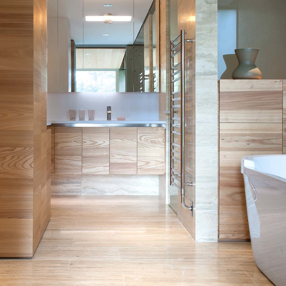 Photo of an expansive modern master bathroom in Vancouver with an undermount sink, flat-panel cabinets, light wood cabinets, engineered quartz benchtops, a freestanding tub, stone tile and travertine floors.