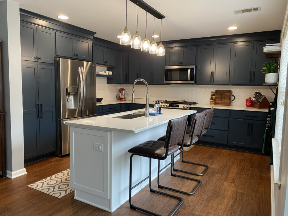 Example of a mid-sized transitional u-shaped brown floor enclosed kitchen design with an undermount sink, shaker cabinets, blue cabinets, quartz countertops, white backsplash, stainless steel appliances, an island and white countertops