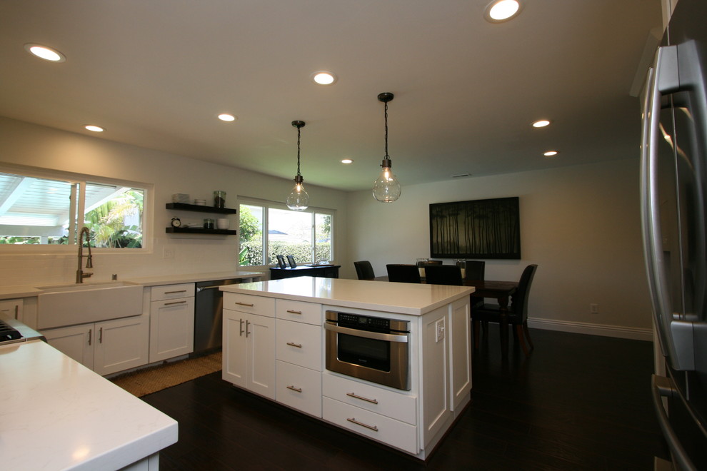 Inspiration for a large transitional u-shaped dark wood floor eat-in kitchen remodel in Orange County with a farmhouse sink, shaker cabinets, white cabinets, quartz countertops, white backsplash, ceramic backsplash, stainless steel appliances and an island
