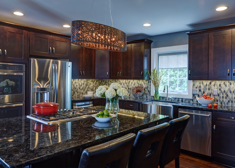Inspiration for an expansive eclectic l-shaped open plan kitchen in Milwaukee with a farmhouse sink, shaker cabinets, dark wood cabinets, granite benchtops, blue splashback, glass tile splashback, stainless steel appliances, dark hardwood floors and with island.
