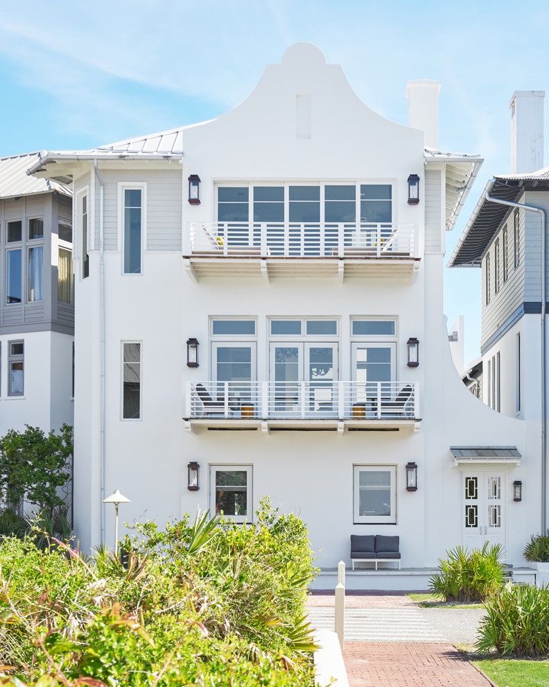 Photo of a large beach style three-storey stucco white house exterior in Other with a metal roof.