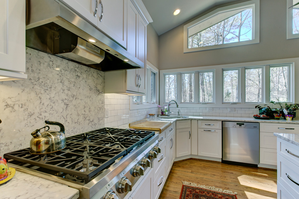 Example of a large transitional u-shaped medium tone wood floor eat-in kitchen design in Raleigh with a single-bowl sink, shaker cabinets, white cabinets, quartz countertops, white backsplash, ceramic backsplash, stainless steel appliances and an island