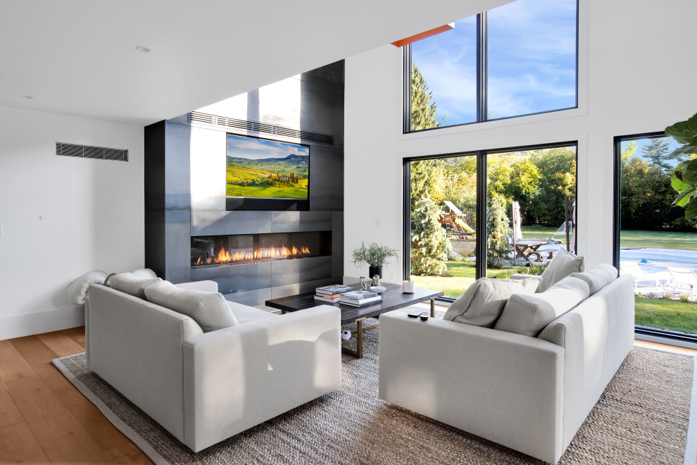 This is an example of a large contemporary open concept living room in Detroit with light hardwood floors, a built-in media wall, a ribbon fireplace and a metal fireplace surround.
