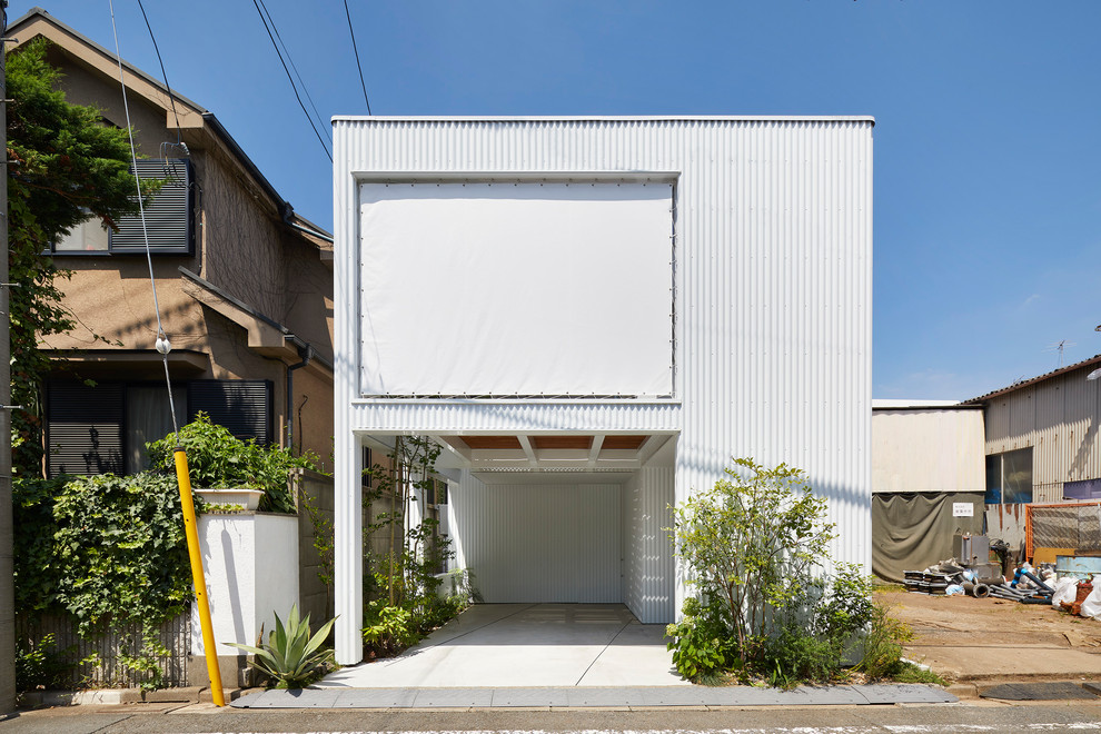 Photo of a small midcentury two-storey white house exterior in Tokyo with metal siding, a flat roof and a metal roof.
