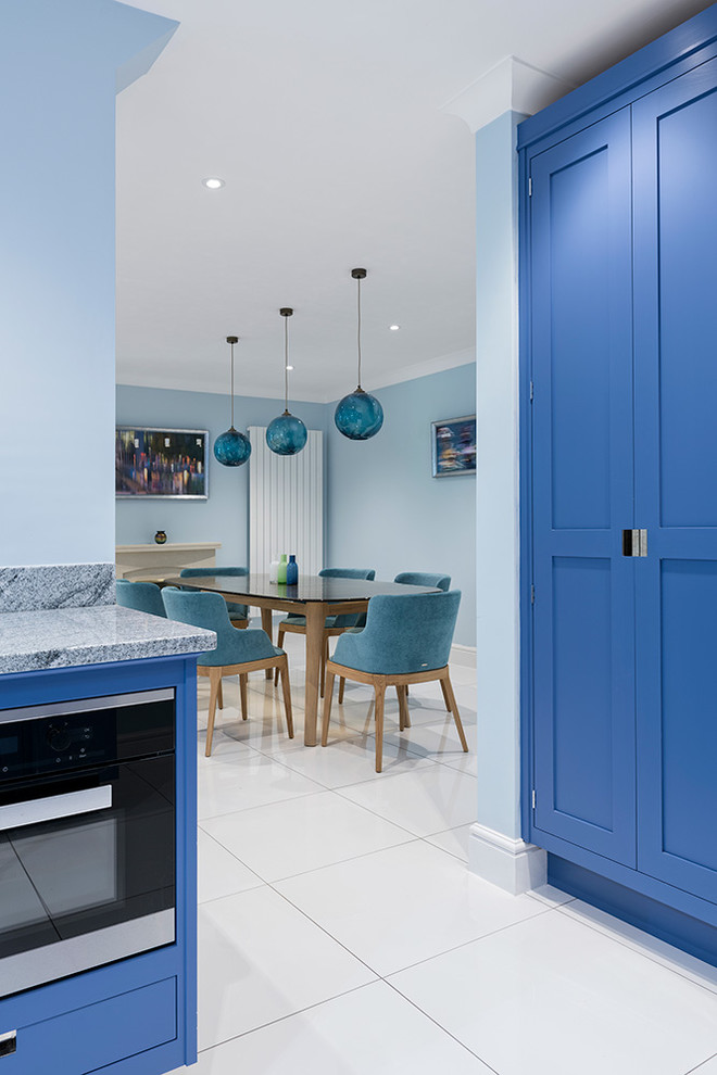 Design ideas for a mid-sized contemporary l-shaped open plan kitchen in Hampshire with a drop-in sink, shaker cabinets, blue cabinets, granite benchtops, grey splashback, marble splashback, white appliances, ceramic floors, with island, white floor and grey benchtop.