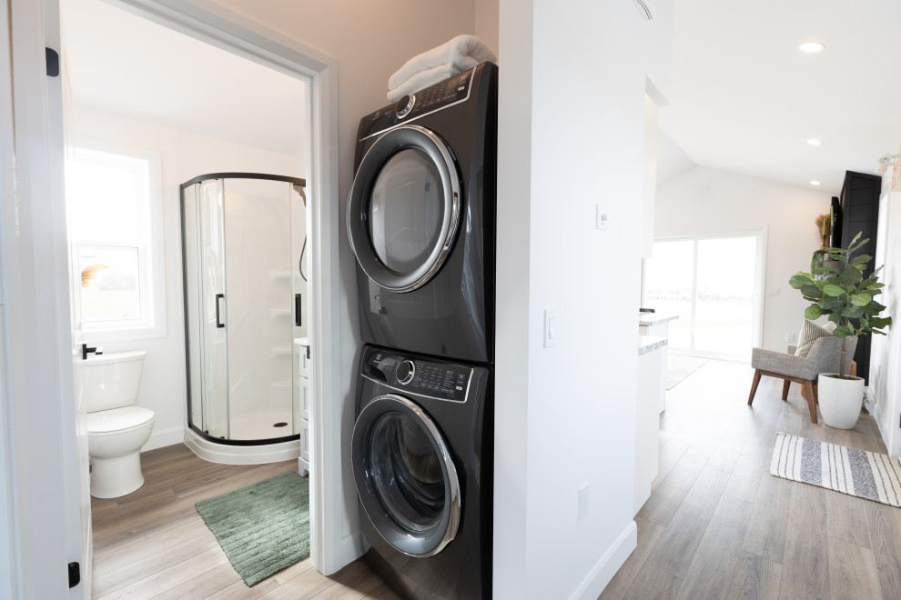 Ejemplo de armario lavadero abovedado minimalista pequeño con paredes blancas, suelo vinílico, lavadora y secadora apiladas y suelo marrón
