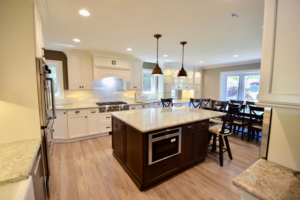 Huge transitional vinyl floor and brown floor eat-in kitchen photo with a farmhouse sink, recessed-panel cabinets, white cabinets, quartz countertops, multicolored backsplash, ceramic backsplash, stainless steel appliances, an island and multicolored countertops