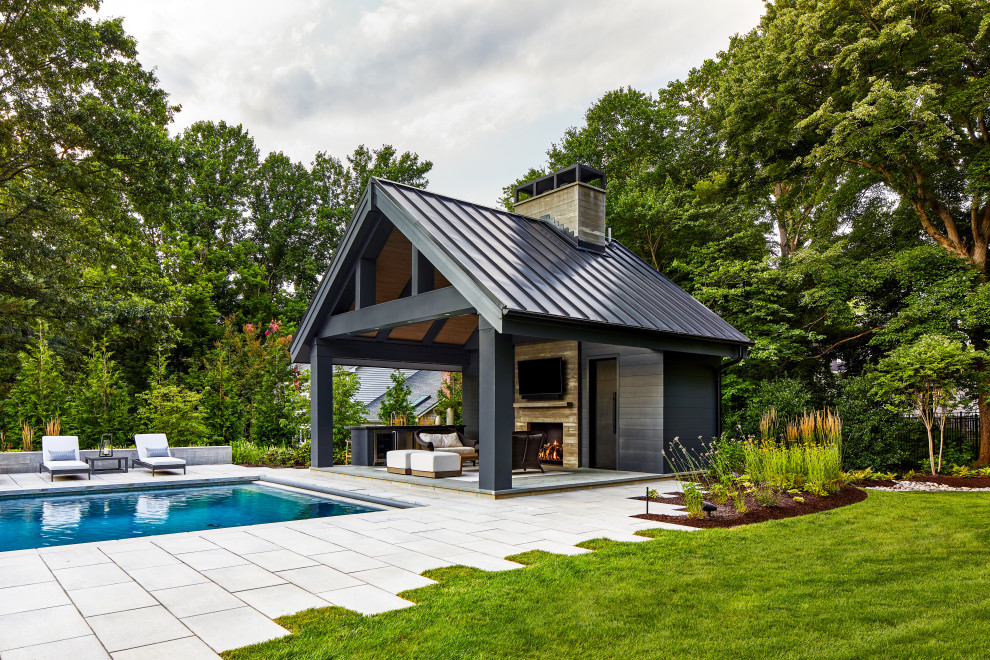 На фото: большой прямоугольный бассейн на заднем дворе с домиком у бассейна и мощением тротуарной плиткой с