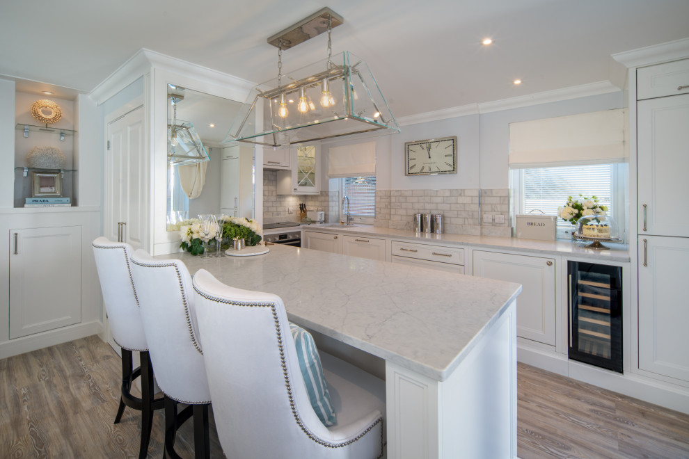 This is an example of a mid-sized beach style u-shaped eat-in kitchen in Other with an undermount sink, shaker cabinets, white cabinets, quartzite benchtops, white splashback, marble splashback, black appliances, a peninsula, grey floor and white benchtop.