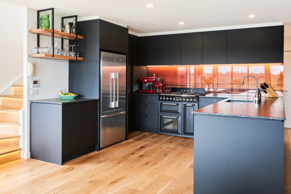 Photo of a mid-sized contemporary u-shaped open plan kitchen in Melbourne with flat-panel cabinets, black cabinets, quartz benchtops, orange splashback, glass sheet splashback, black appliances and black benchtop.