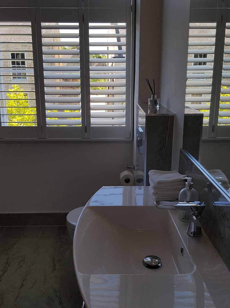 Photo of a large contemporary bathroom in Other with flat-panel cabinets, white cabinets, a freestanding bath, a wall mounted toilet, grey tiles, porcelain tiles, grey walls, porcelain flooring, a wall-mounted sink, marble worktops, grey floors, an open shower and white worktops.