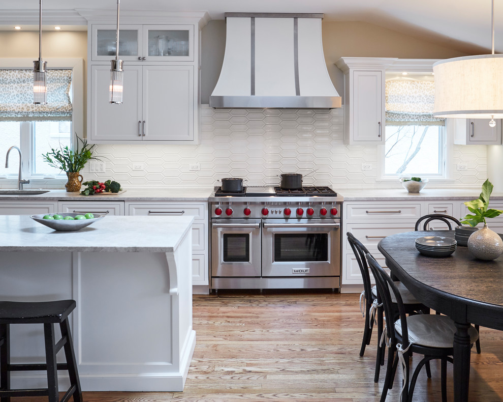 Mid-sized transitional l-shaped medium tone wood floor eat-in kitchen photo in Chicago with a double-bowl sink, flat-panel cabinets, white cabinets, marble countertops, white backsplash, porcelain backsplash, stainless steel appliances, an island and gray countertops