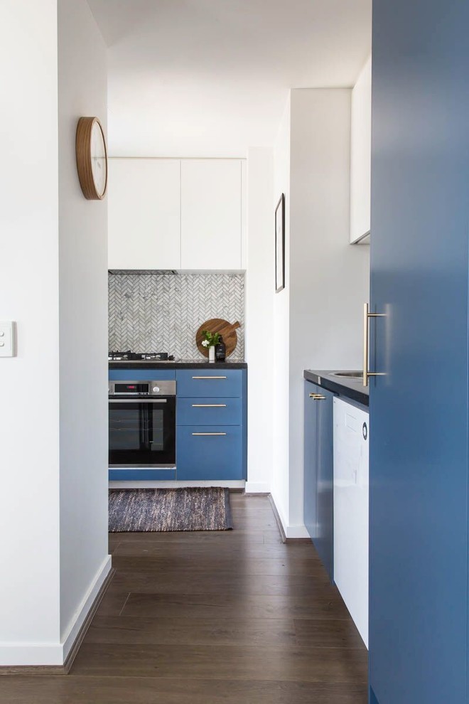 This is an example of a small contemporary l-shaped kitchen pantry in Melbourne with a single-bowl sink, blue cabinets, granite benchtops, grey splashback, mosaic tile splashback, stainless steel appliances, laminate floors, no island, brown floor and black benchtop.