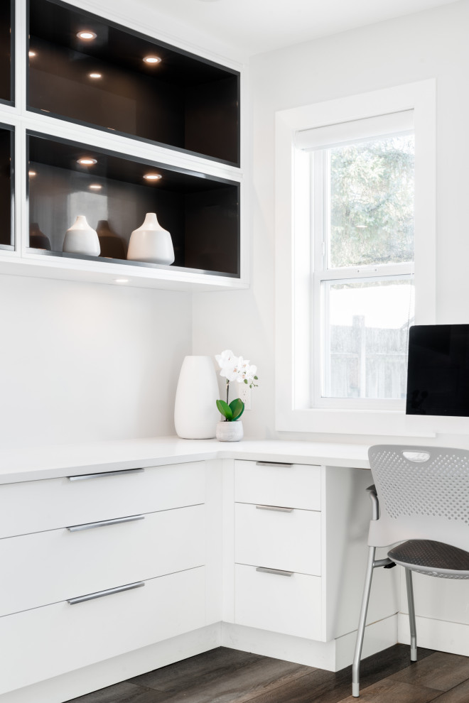 Photo of a mid-sized modern home office in Vancouver with white walls, vinyl floors, a standard fireplace, a plaster fireplace surround, a built-in desk and brown floor.