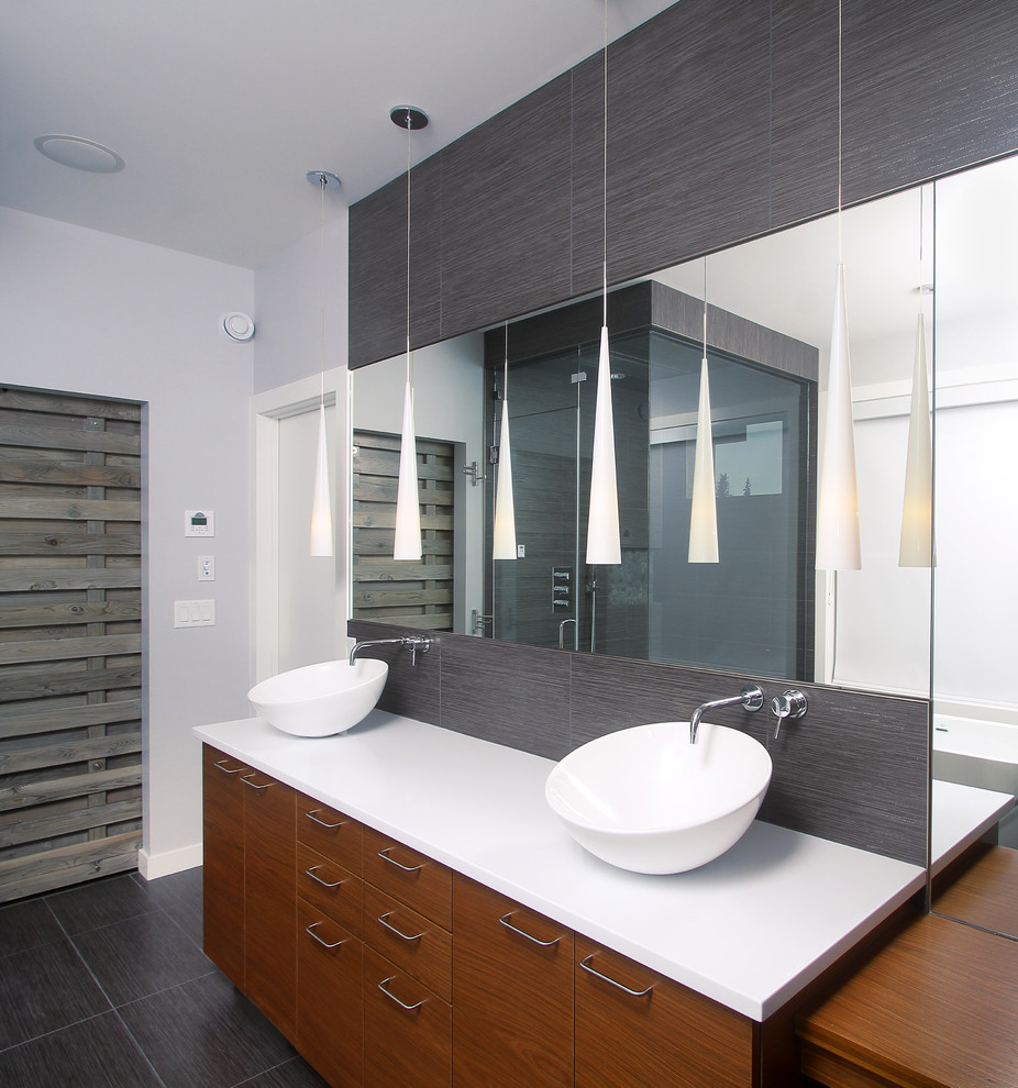Mid-sized contemporary master bathroom in Edmonton with a vessel sink, flat-panel cabinets, gray tile, grey walls, porcelain tile, porcelain floors, solid surface benchtops, grey floor, medium wood cabinets, a freestanding tub, a corner shower, a hinged shower door and white benchtops.