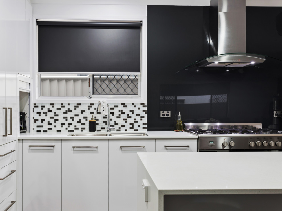 Mid-sized modern eat-in kitchen in Gold Coast - Tweed with flat-panel cabinets, white cabinets, laminate benchtops, black splashback, glass sheet splashback, stainless steel appliances, with island and white benchtop.