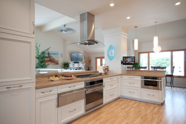 This is an example of a large beach style galley open plan kitchen in San Diego with an undermount sink, recessed-panel cabinets, white cabinets, solid surface benchtops, beige splashback, stone tile splashback, stainless steel appliances and no island.