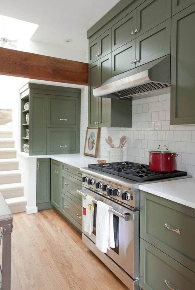 Large transitional l-shaped light wood floor and brown floor eat-in kitchen photo in Columbus with a farmhouse sink, recessed-panel cabinets, green cabinets, quartz countertops, white backsplash, ceramic backsplash, stainless steel appliances, an island and white countertops