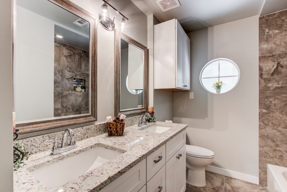 This is an example of a mid-sized traditional 3/4 bathroom in Houston with shaker cabinets, white cabinets, an alcove tub, a shower/bathtub combo, a one-piece toilet, gray tile, ceramic tile, grey walls, ceramic floors, an undermount sink, granite benchtops, multi-coloured floor, a shower curtain and multi-coloured benchtops.