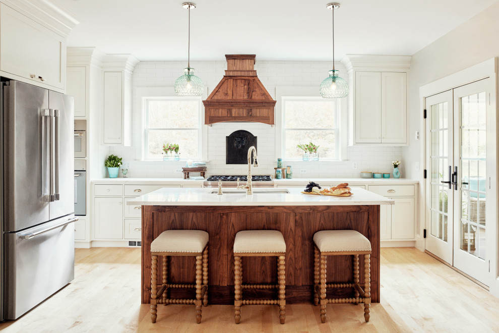 Large country eat-in kitchen in Portland Maine with a single-bowl sink, shaker cabinets, white cabinets, quartz benchtops, white splashback, ceramic splashback, stainless steel appliances, light hardwood floors, with island and white benchtop.