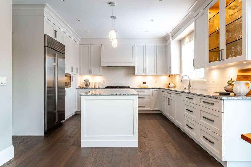 Example of a large transitional u-shaped medium tone wood floor and brown floor eat-in kitchen design in Vancouver with an undermount sink, white cabinets, granite countertops, white backsplash, subway tile backsplash, stainless steel appliances, an island, multicolored countertops and shaker cabinets