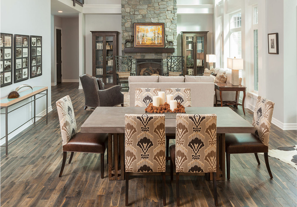 This is an example of a mid-sized transitional open plan dining in Detroit with grey walls, dark hardwood floors, a standard fireplace, a stone fireplace surround and brown floor.