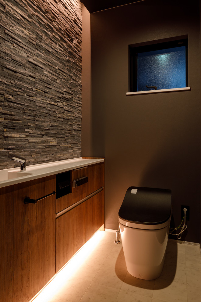 Exempel på ett litet vit vitt toalett, med luckor med profilerade fronter, skåp i mellenmörkt trä, en toalettstol med hel cisternkåpa, grå kakel, stenkakel, svarta väggar, vinylgolv, bänkskiva i akrylsten och vitt golv