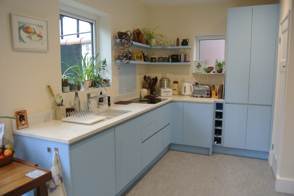Esempio di una cucina a L moderna chiusa e di medie dimensioni con lavello da incasso, ante lisce, ante bianche, top in vetro riciclato, paraspruzzi blu, paraspruzzi con lastra di vetro, elettrodomestici neri e top bianco