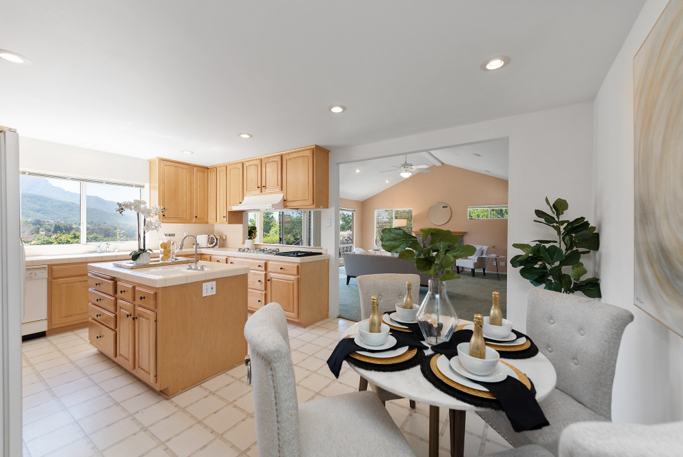 Photo of a mid-sized country u-shaped eat-in kitchen in Los Angeles with a drop-in sink, raised-panel cabinets, light wood cabinets, tile benchtops, ceramic splashback, white appliances, laminate floors, with island, white floor, white benchtop and wood.