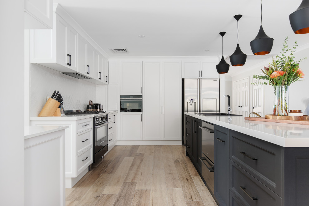 Photo of a large transitional galley kitchen in Perth with a double-bowl sink, shaker cabinets, white cabinets, quartz benchtops, white splashback, ceramic splashback, black appliances, with island and white benchtop.