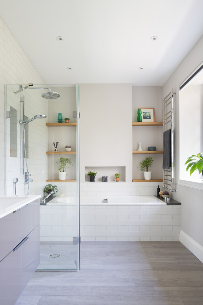 Inspiration for a mid-sized contemporary wet room bathroom in Other with flat-panel cabinets, a drop-in tub, white tile, subway tile, grey walls, laminate floors, a wall-mount sink, grey floor and an open shower.