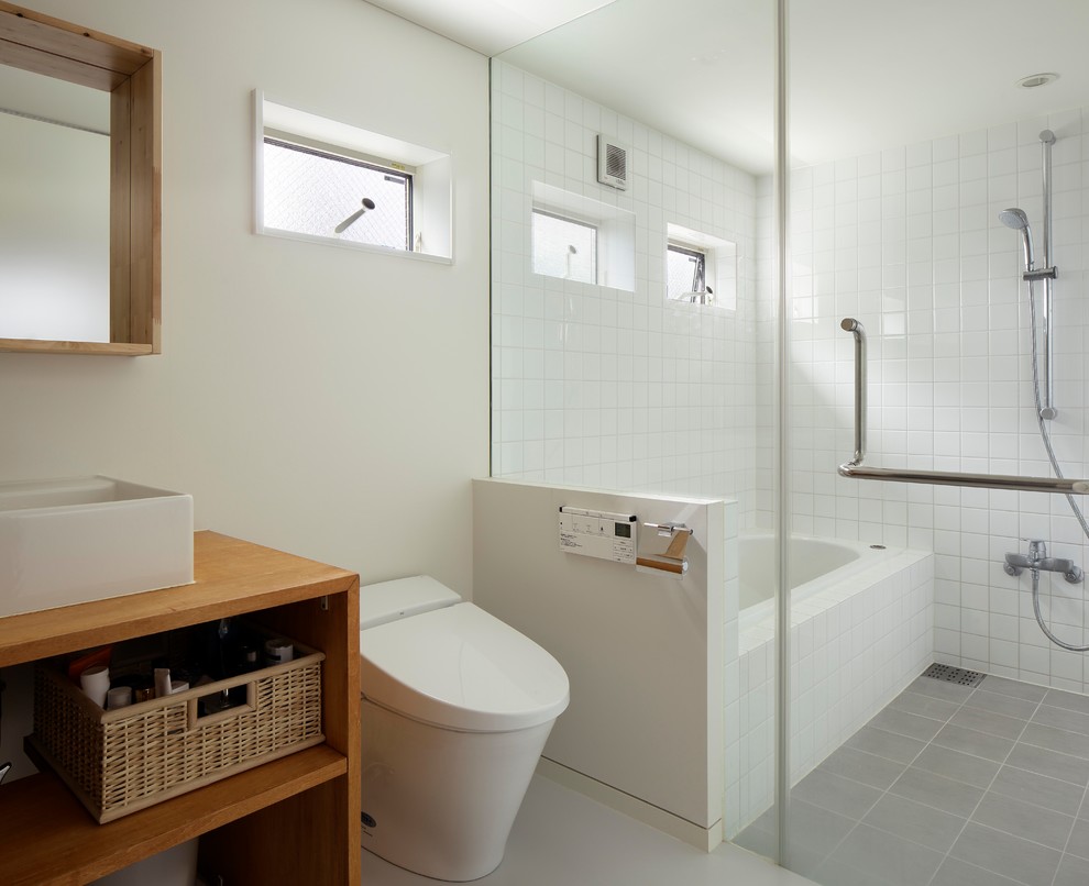 This is an example of a small contemporary master bathroom in Yokohama with medium wood cabinets, an undermount tub, a one-piece toilet, white walls, porcelain floors, a vessel sink and grey floor.