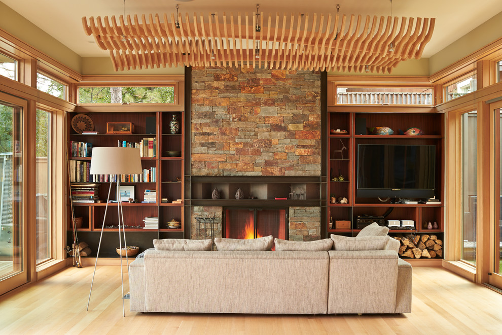 This is an example of a mid-sized contemporary open concept family room in Other with light hardwood floors, a standard fireplace, a built-in media wall, a library and beige walls.