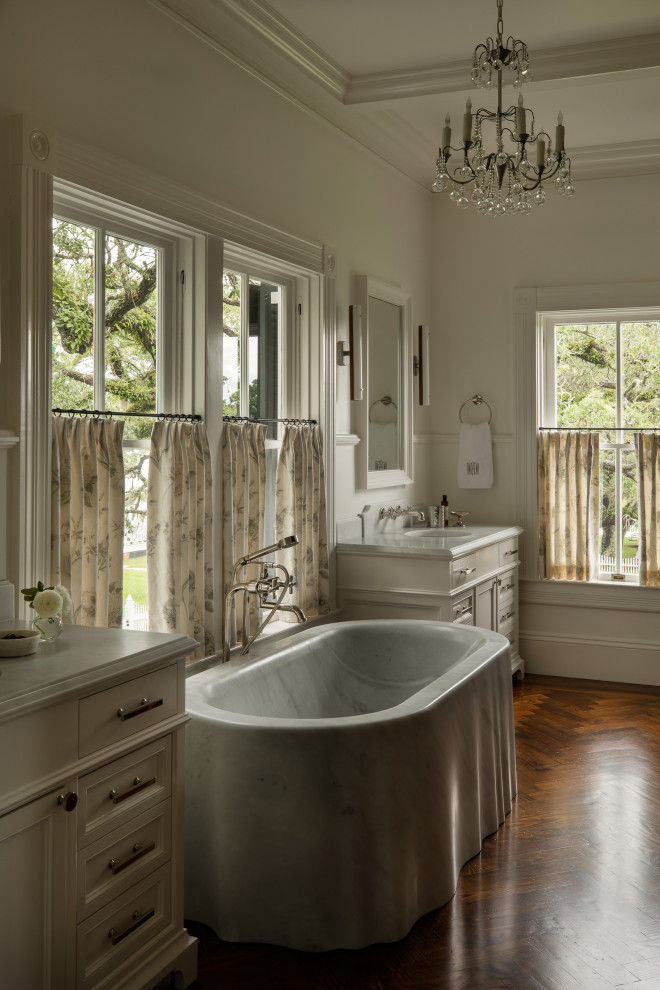 Idéer för att renovera ett stort vintage vit vitt en-suite badrum, med luckor med profilerade fronter, vita skåp, ett fristående badkar, vita väggar, mörkt trägolv, ett integrerad handfat, marmorbänkskiva och brunt golv