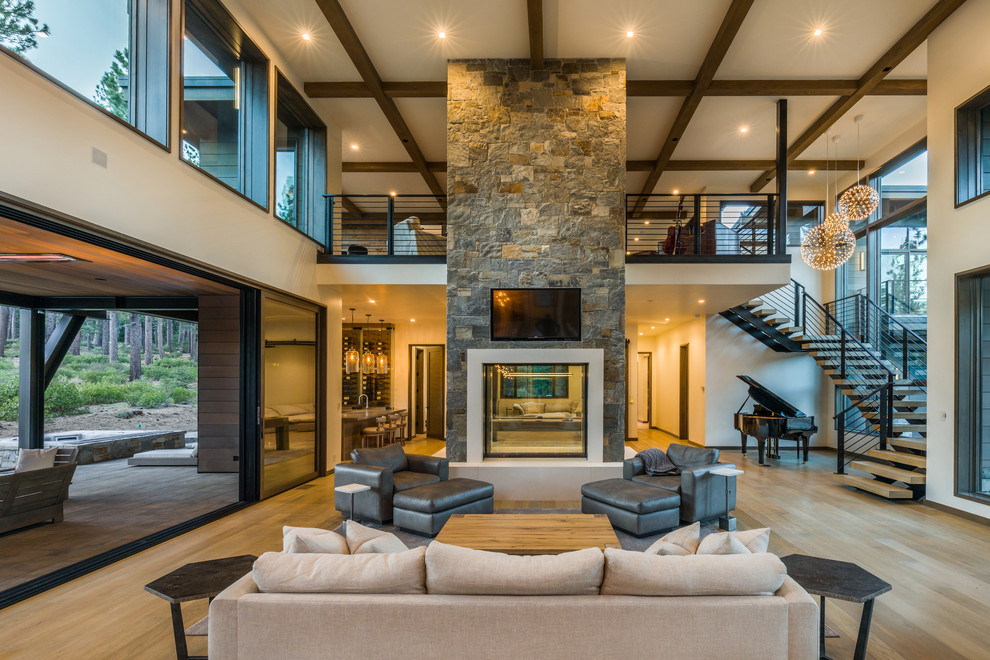 Photo of a large contemporary open concept living room in Sacramento with white walls, light hardwood floors, a two-sided fireplace, a concrete fireplace surround, a wall-mounted tv, brown floor and a music area.