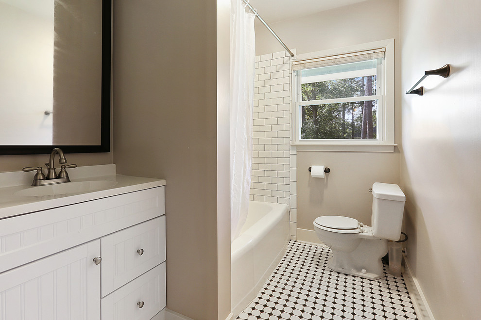 This is an example of a mid-sized midcentury kids bathroom in New Orleans with beaded inset cabinets, white cabinets, an alcove tub, a shower/bathtub combo, a two-piece toilet, white tile, glass tile, grey walls, porcelain floors, an integrated sink, marble benchtops, multi-coloured floor and a shower curtain.