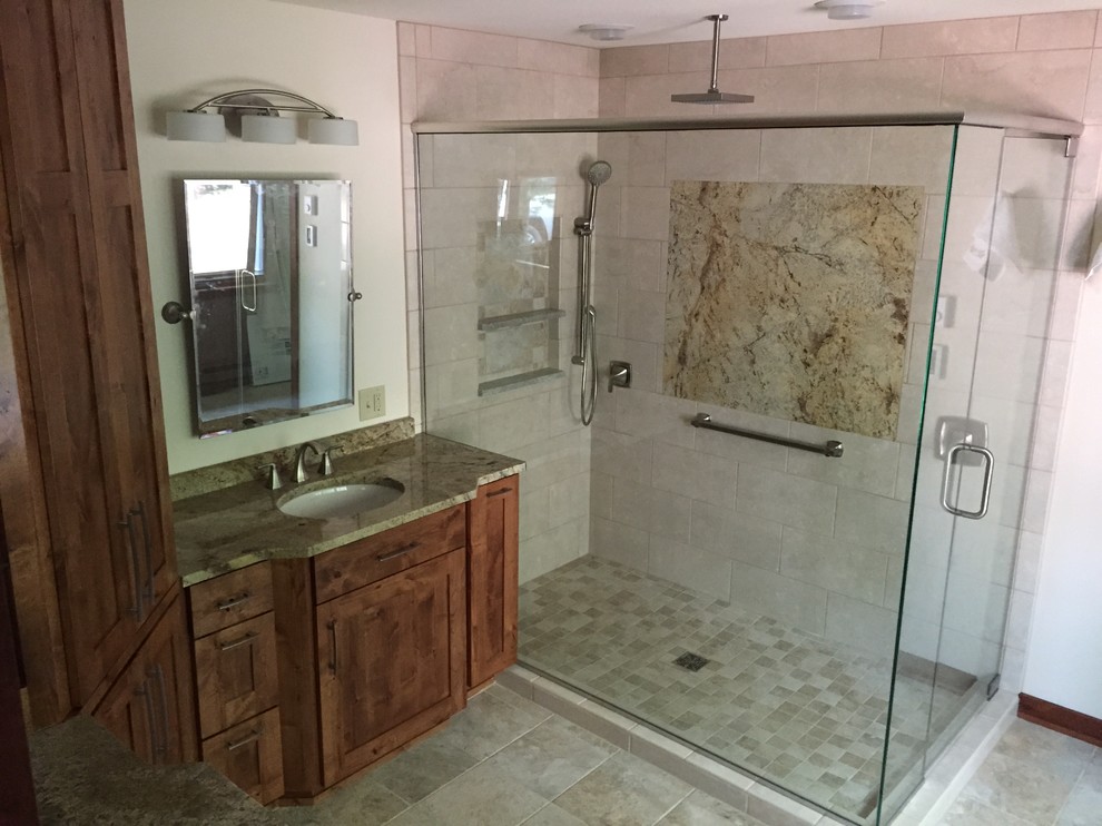 Transitional corner shower photo with recessed-panel cabinets, medium tone wood cabinets, an undermount sink and granite countertops